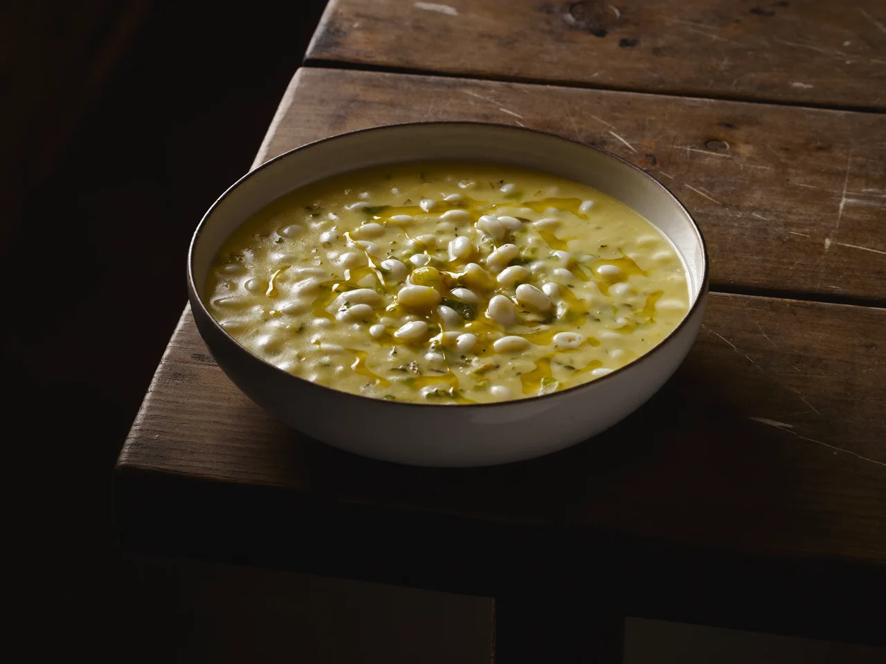 Ciotola profonda di minestrina vellutata con pastina e filo d'olio su legno rustico