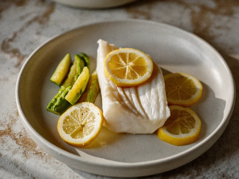 Filetto di pesce bianco al forno con limone e zucchine al vapore su piatto di gres
